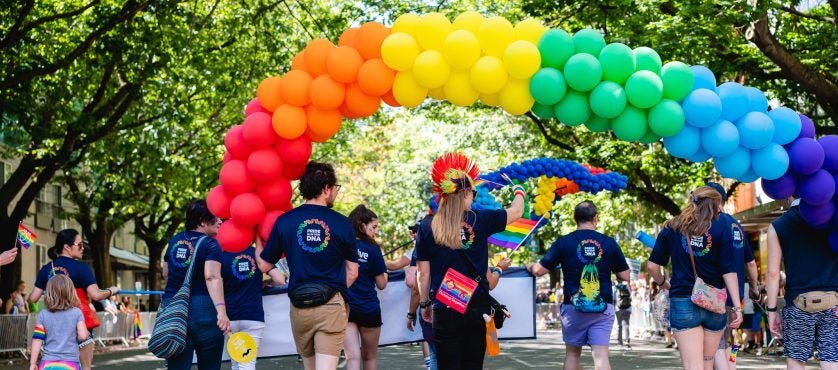 Adaptive Volunteers march in the PRIDE parade under a balloon arch